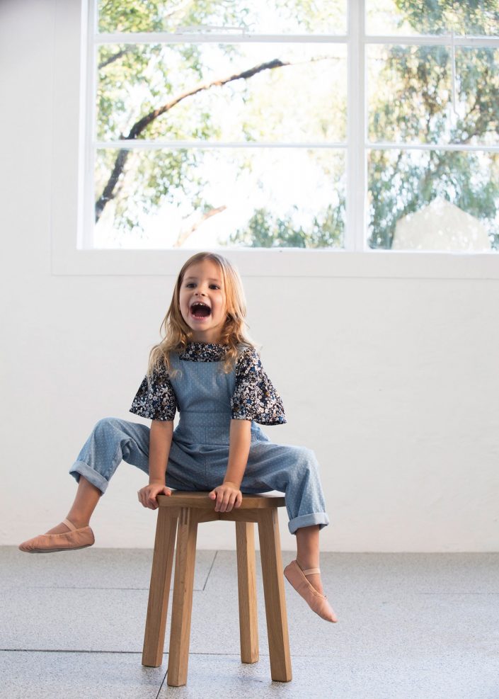 young girl on wooden stool wearing denim overalls